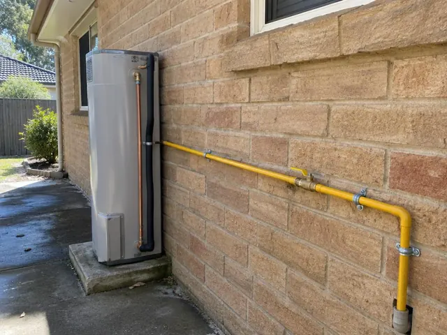 Yellow gas pipe and fittings running along a brick exterior wall beside a hot water unit in Thornleigh