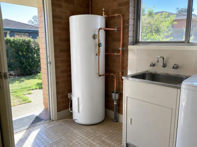 White hot water cylinder beside a sink in a tiled laundry with brick walls in Westleigh